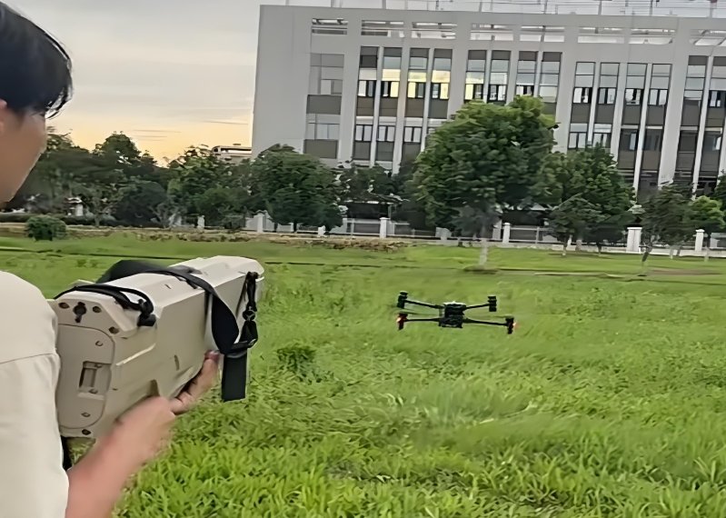 Man using a handheld drone jamming device to target a flying quad - copter drone in an open grassy area